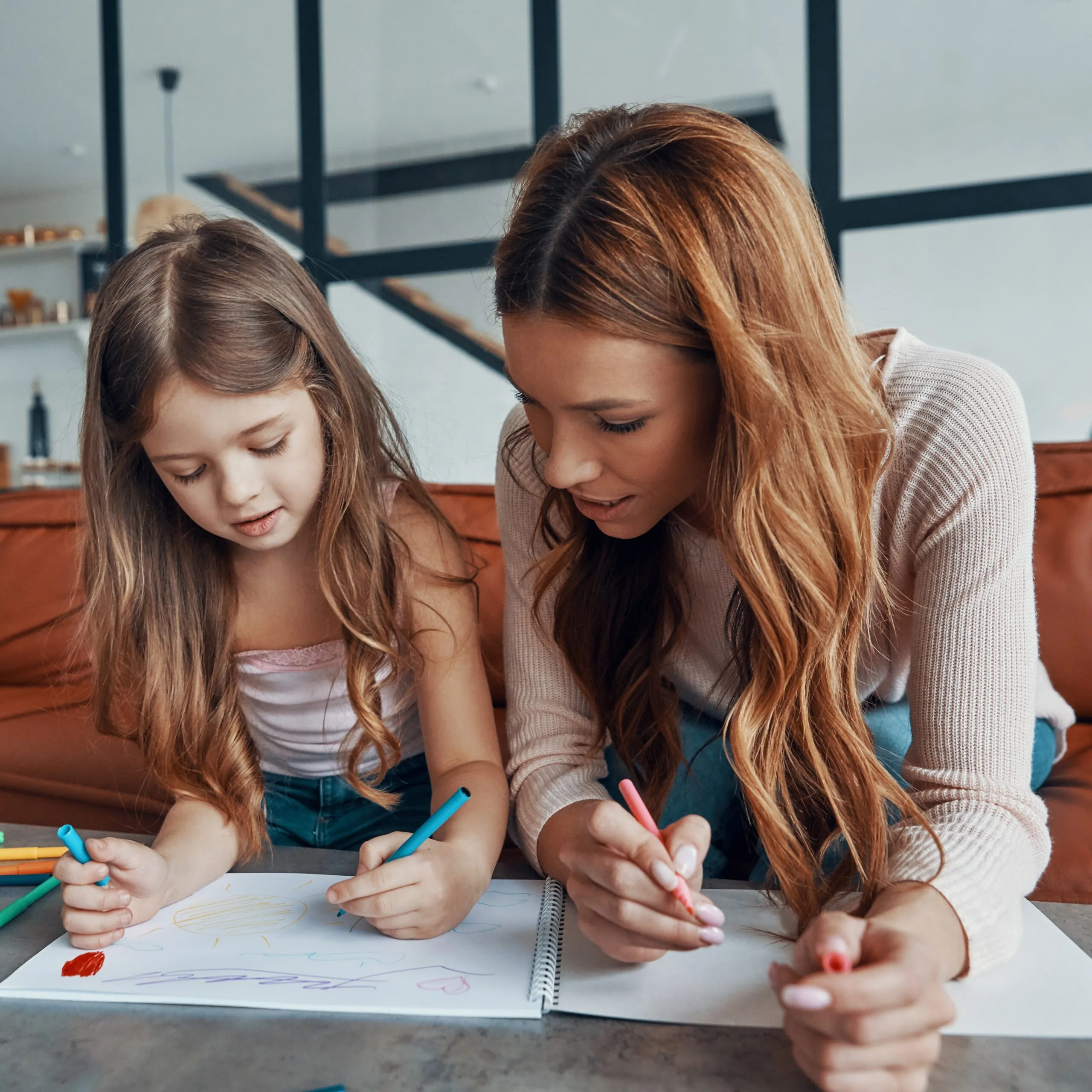 Young beautiful mother and her little daughter drawing in sketchbook while spending time at home